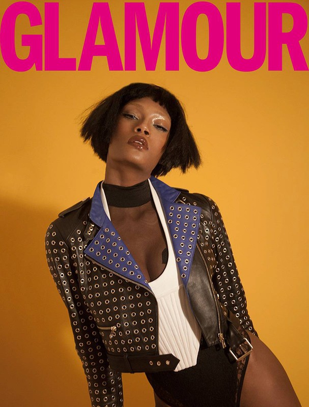 Glamour cover featuring a stylish black woman with short hair, wearing a studded jacket and bodysuit, against a yellow backdrop.
