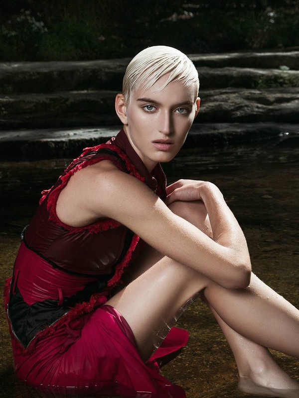 Model with slicked-back blonde hair wearing a maroon dress seated near water in Los Angeles