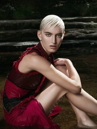 Model with slicked-back blonde hair wearing a maroon dress seated near water in Los Angeles