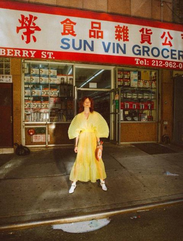 Woman in yellow dress stands in front of Sun Vin Grocery store in New York City at night, illuminated by street lights.