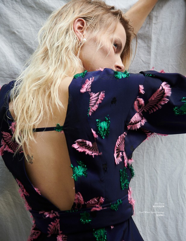 Young woman in elegant navy dress with pink and green leaf embellishments poses on a gray sheet, showcasing a stylish and sophisticated look.