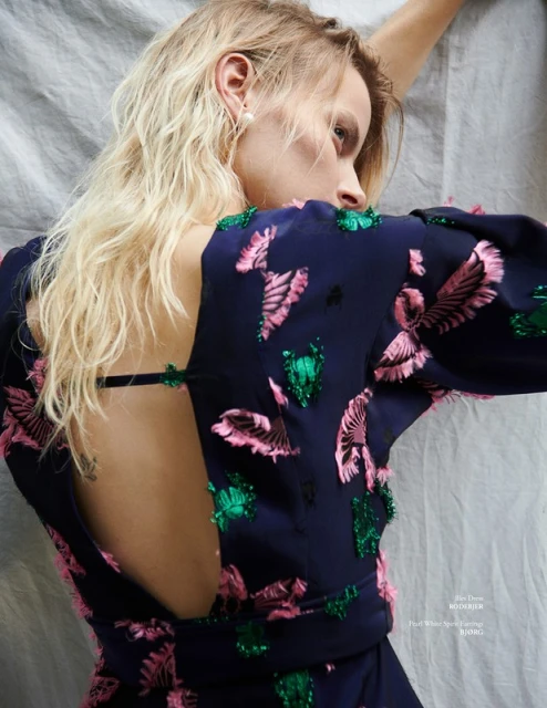Young woman in elegant navy dress with pink and green leaf embellishments poses on a gray sheet, showcasing a stylish and sophisticated look.