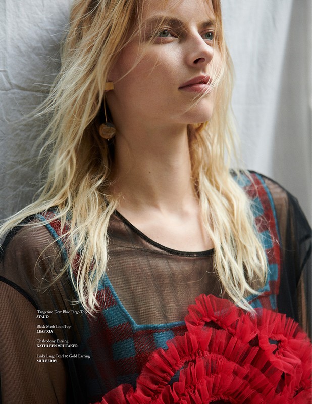 Blonde woman in sheer black top with red flower detail, facing right with soft diffused lighting. Fashion editorial style photograph.
