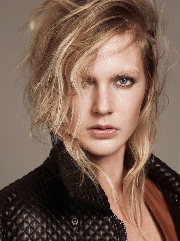 Close-up portrait of a blonde woman in a black leather jacket against a neutral background, showcasing a fashion-forward and edgy aesthetic.