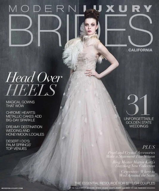Modern Luxury Brides magazine cover featuring a woman in a wedding gown, feathered collar, and elegant updo against a gray backdrop.