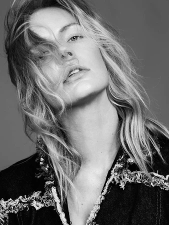 Black and white portrait of a woman with light, wavy hair wearing a fringed denim jacket against a neutral background in a studio.