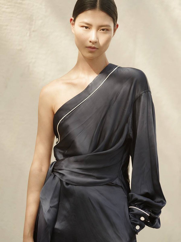 Portrait of a woman in a navy blue, one-shoulder dress with white trim against a neutral background, fashion photography, studio lighting.