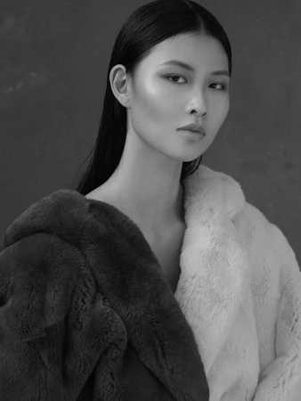 Portrait of an Asian woman with sleek dark hair wearing a plush textured coat against a dark background