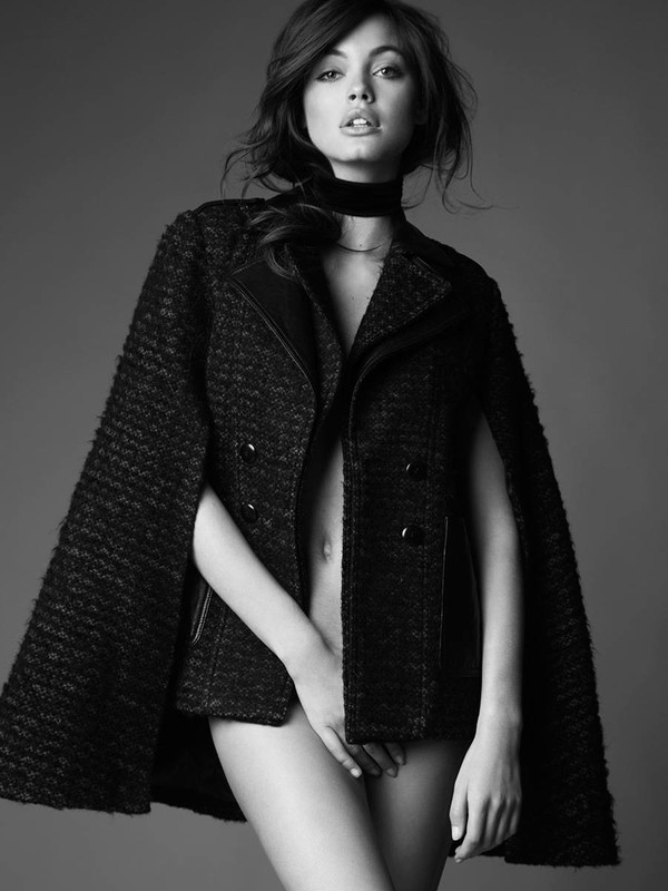 Monochrome portrait of a woman wearing a jacket with hand covering lower body, against a grey background. Fashion advertisement.