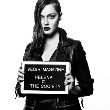 Black and white portrait of a woman in a leather jacket holding a letter board sign against a plain white background
