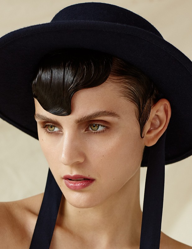 Close-up portrait of a woman wearing a black hat and styled wet-look finger waves with neutral background