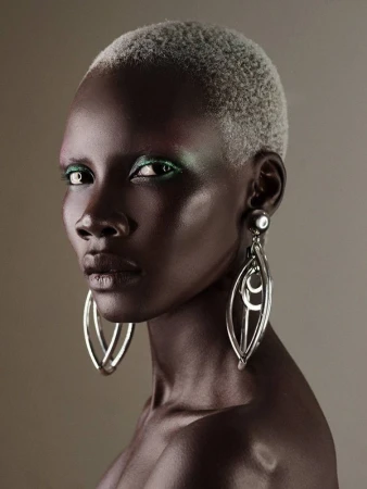 Close-up portrait of a Black woman with short frosted hair, metallic silver hoop earrings, and vibrant green eyeshadow.