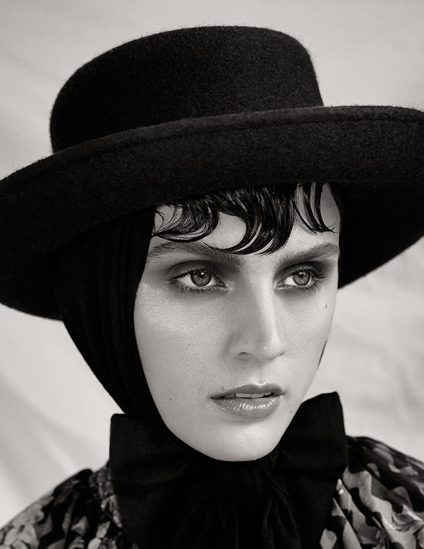 Close-up portrait of a woman wearing a wide-brimmed black hat and dark clothing with wet-style bangs.