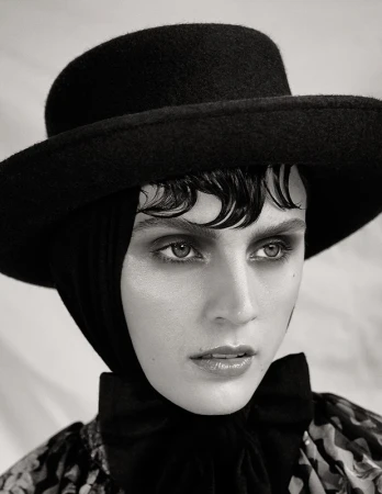 Close-up portrait of a woman wearing a wide-brimmed black hat and dark clothing with wet-style bangs.