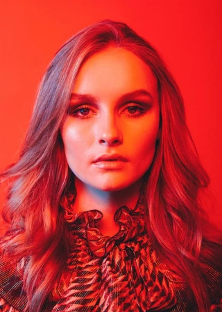 Portrait of an adult female model with long wavy hair in a printed top, brightly lit with red and blue gel lighting in a photo studio.
