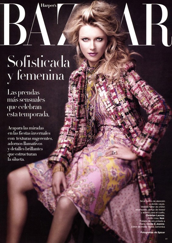 Fashion magazine cover featuring a blonde model in a patterned dress and coat, posing indoors with dark background and magazine text.