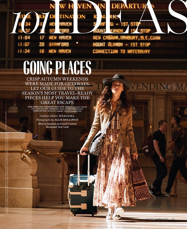 Editorial fashion shot of woman with luggage in a train station with arrival and departure boards, natural lighting, stylish travel attire.