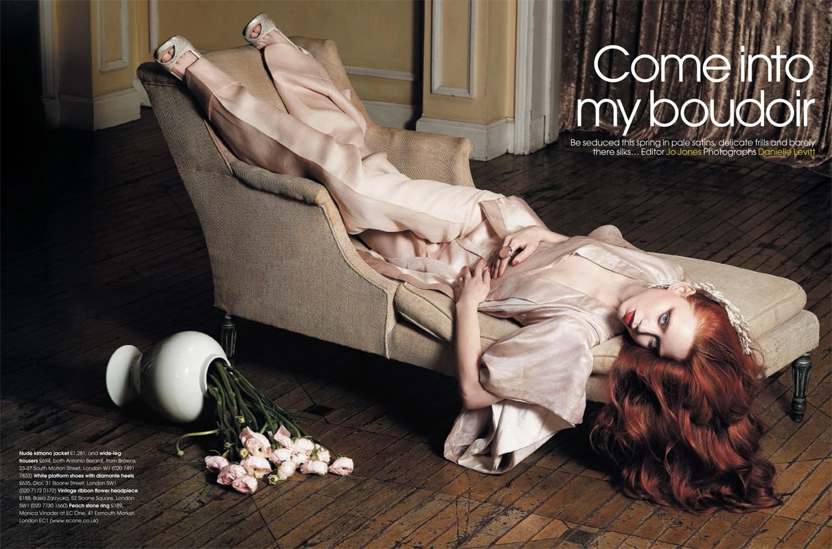 A woman with red hair in a pale satin robe reclines on a chaise lounge with flowers spilling from a vase on the floor.