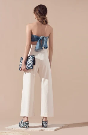 Rear view of a model in a blue strapless top, white trousers, and platform shoes holding a patterned clutch.
