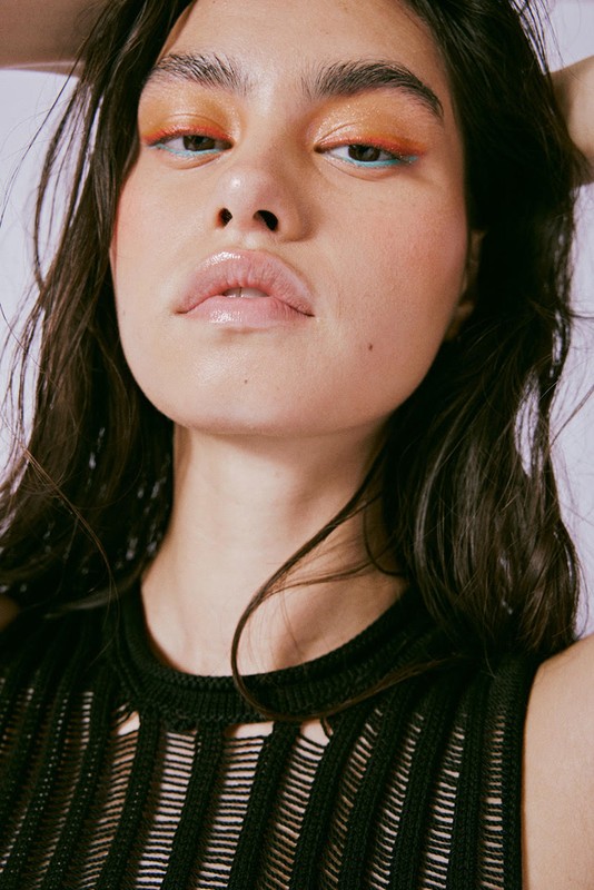 Close-up shot of a woman with brown hair wearing makeup and a black, see-through shirt against a white background in a studio setting.