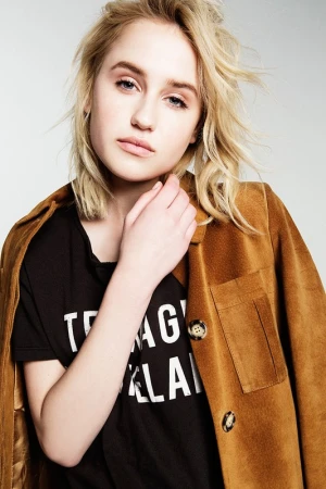 Close-up portrait of a blonde woman wearing a black t-shirt and brown jacket against a white background