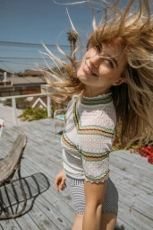 Blonde woman with blowing hair wearing striped knit top on wooden rooftop deck in Los Angeles by Samantha Fryling