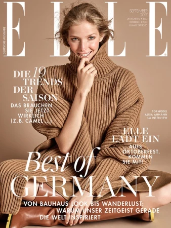 Smiling female model wearing a thick camel turtleneck sweater and brown boots against a plain background.