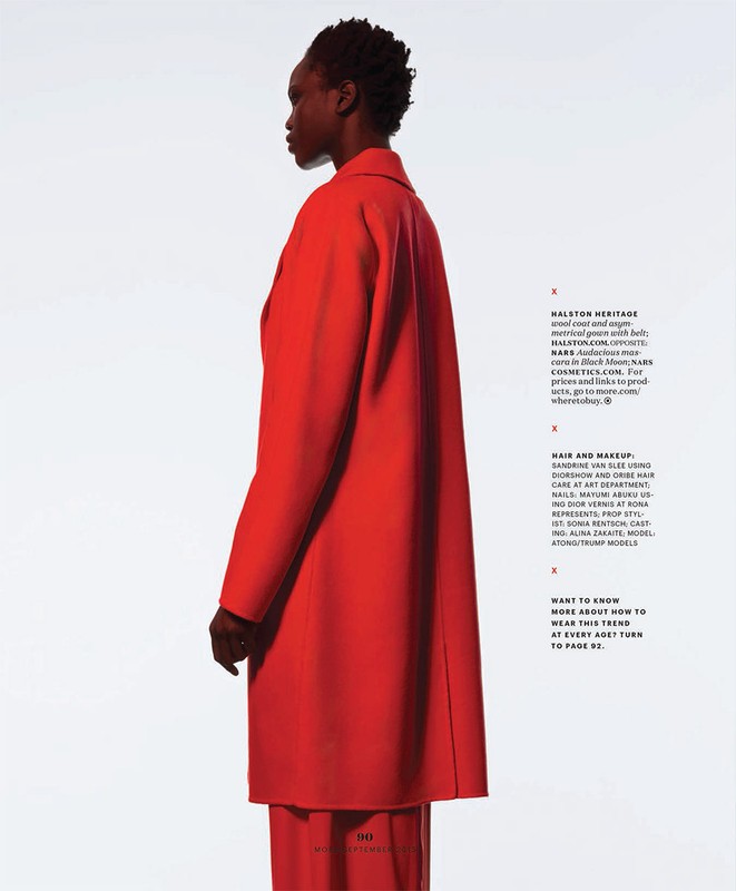 A stylish fashion editorial shot featuring an African American woman in a bold red overcoat and matching pants against a white backdrop.