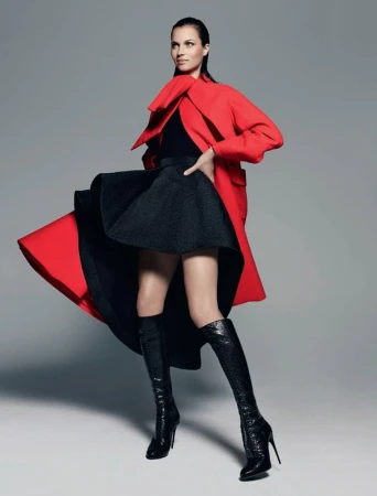 Model in red coat and black skirt wearing knee-high boots against a grey seamless background