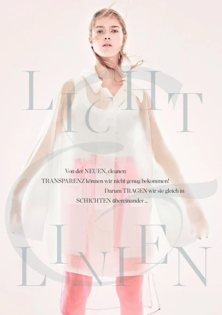 Woman in a sheer top, transparent dress with light pink lining, standing in a light pink room in a fashion editorial photoshoot.