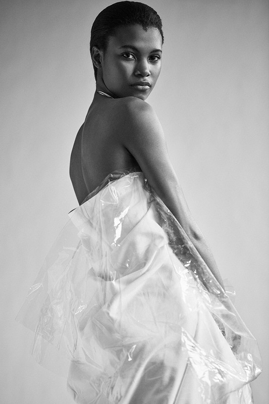 Black and white portrait of an African-American woman wearing a clear plastic garment in a studio with neutral lighting.