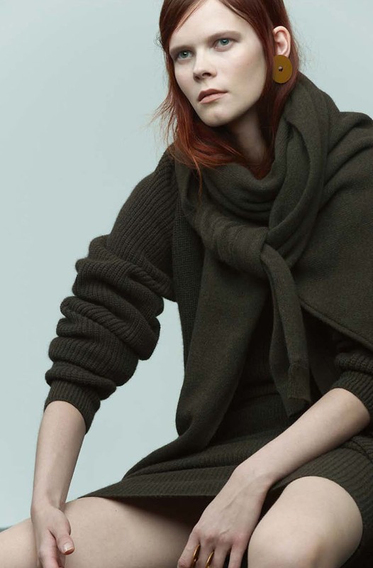 Adult woman with auburn hair poses in a photo studio wearing a dark green sweater dress and matching scarf, with a neutral backdrop.