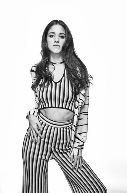 Portrait of a young adult woman with long brown hair wearing a vertically striped knit outfit against a white background in studio light.