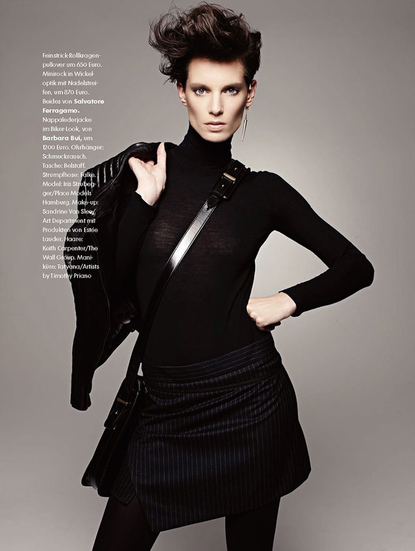Fashionable woman in black turtleneck, mini skirt, and jacket poses in a studio, showcasing edgy and stylish look with dark makeup.