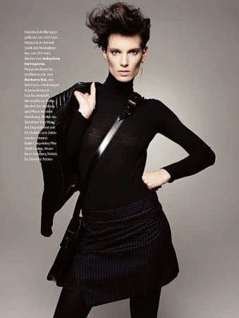 Fashionable woman in black turtleneck, mini skirt, and jacket poses in a studio, showcasing edgy and stylish look with dark makeup.