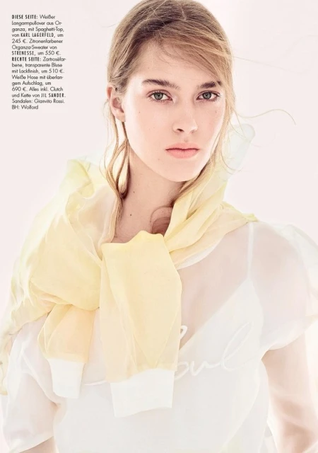 Fashion editorial portrait of a young fair-skinned woman wearing a sheer white top and a yellow organza scarf in a studio setting.