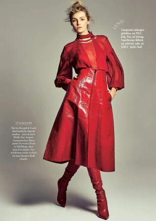 A female model wearing a red silk blouse, red leather skirt, and matching red boots against a grey seamless studio background.