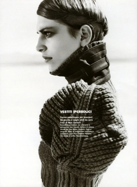 Black and white fashion portrait of a slender adult woman in a thick knit sweater and leather collar in a bright, overcast outdoor setting.