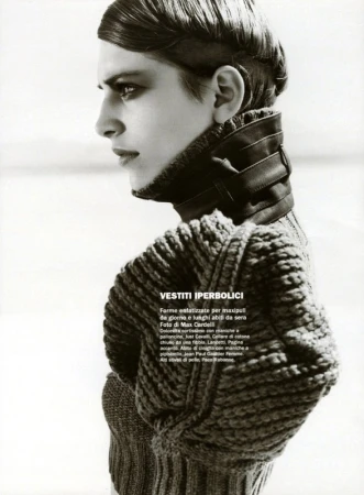 Black and white fashion portrait of a slender adult woman in a thick knit sweater and leather collar in a bright, overcast outdoor setting.