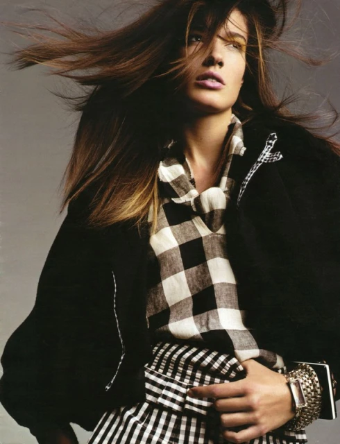 Fashion editorial portrait of a brunette adult woman wearing a black jacket and black and white checkered pattern shirt and skirt.