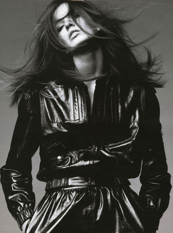 Monochrome portrait of a woman with long brown hair blowing, wearing a black leather jacket and skirt in a fashion editorial.