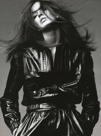 Monochrome portrait of a woman with long brown hair blowing, wearing a black leather jacket and skirt in a fashion editorial.