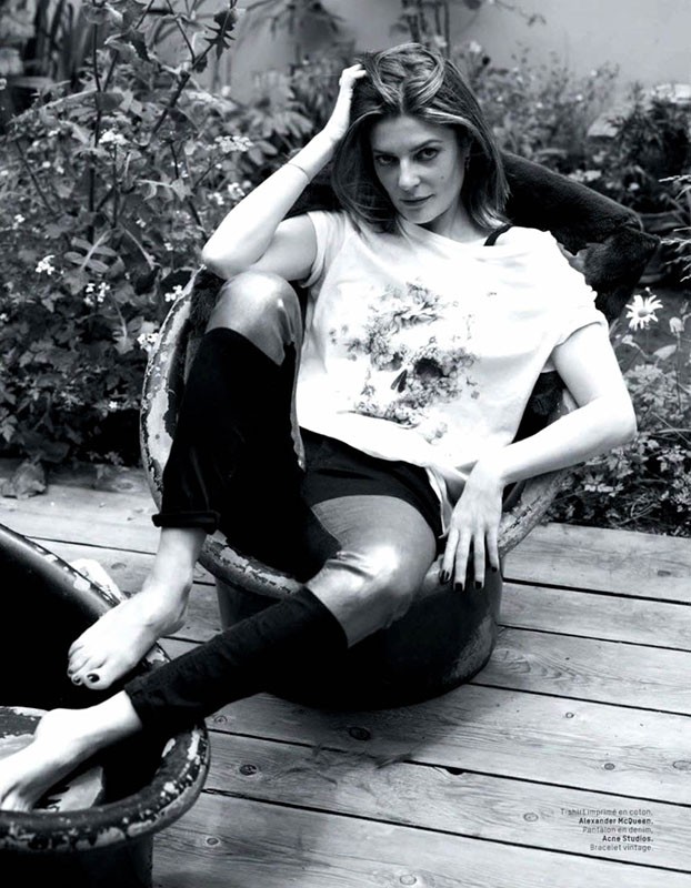 Monochrome shot of a woman with medium-length hair sitting in a metal tub outdoors in a t-shirt, shorts and high socks.