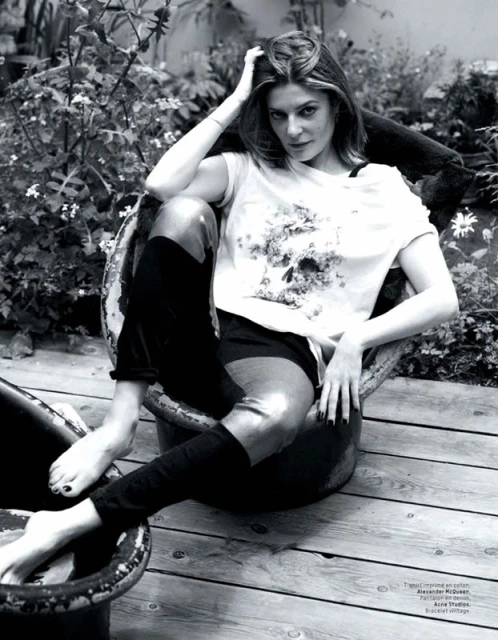 Monochrome shot of a woman with medium-length hair sitting in a metal tub outdoors in a t-shirt, shorts and high socks.