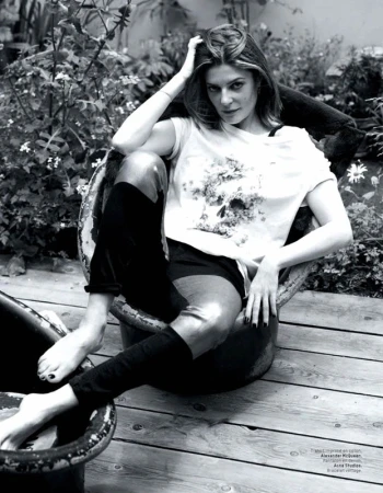 Monochrome shot of a woman with medium-length hair sitting in a metal tub outdoors in a t-shirt, shorts and high socks.