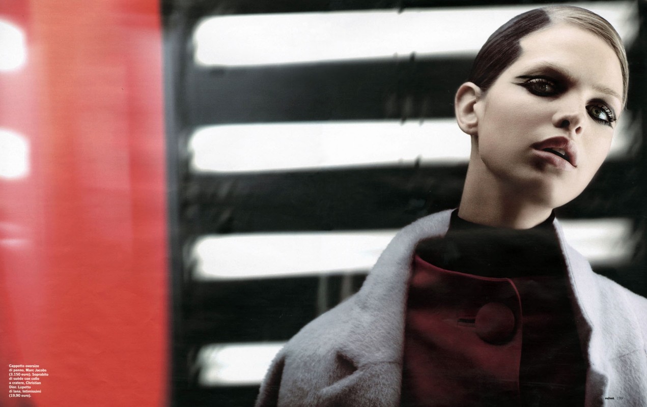 Fashion editorial shot featuring a model in red and gray clothing with dramatic eye makeup, posing against a blurred backdrop.