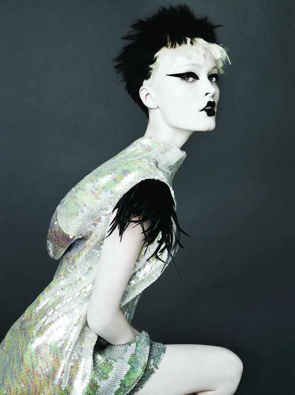 Fashionable person with dramatic black and white hair and makeup wears a shimmering iridescent sequined dress with black feathers.