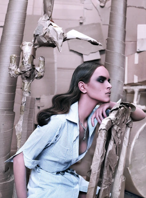 Elegant woman poses in fashion shot with blue-striped shirt and cardboard studio props, showcasing artistic style and photographic technique.