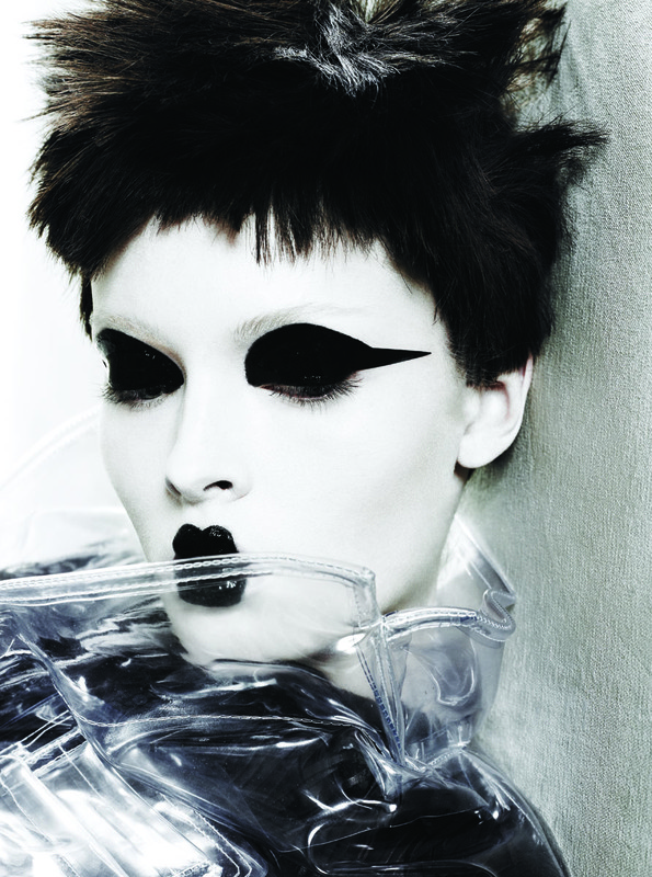 Close-up of a person with stark black and white makeup, featuring dramatic eye makeup, black lipstick, and a clear plastic garment.