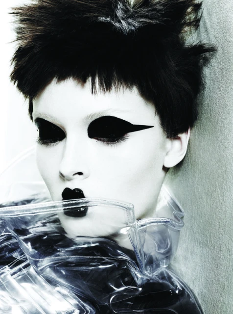 Close-up of a person with stark black and white makeup, featuring dramatic eye makeup, black lipstick, and a clear plastic garment.